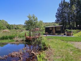 A small black cabin with wooden doors near a wooden deck and pond in a grassy rural area at Celyn in Bontddu near Dolgellau