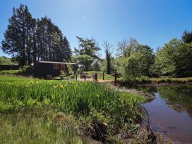 A small black cabin near a pond with yellow flowers and tall trees at Celyn in Bontddu near Dolgellau