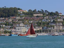 A sailboat with a red sail in a marina with houses on a hill at 2 Court Cottage, Hillfield Village Dartmouth