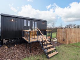 An outdoor view of a black shepherds hut with stairs and a small wooden deck with table and chairs at Shepherds Hut - Oak in Temple Bruer near Lincoln