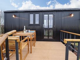 An outdoor wooden deck with a table and chairs outside a black corrugated metal building at Shepherds Hut - Oak in Temple Bruer near Lincoln