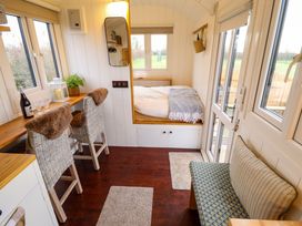 A small room with a bed, two chairs at a counter, a small sofa bench, and multiple windows at Shepherds Hut - Oak in Temple Bruer near Lincoln