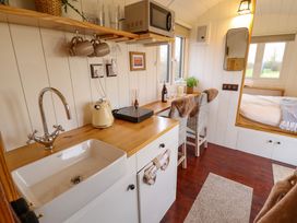 A small kitchen area with a sink kettle microwave and two chairs at a counter with a bed visible in the background at Shepherds Hut - Oak Temple Bruer near Lincoln
