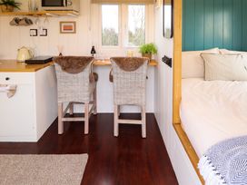 A kitchen area with two wicker chairs at a wooden counter by a window and a bed with cushions in Shepherds Hut Oak in Temple Bruer near Lincoln