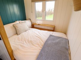 A bed with pillows and a blanket near a window with a wooden shelf beneath it at Shepherds Hut - Oak in Temple Bruer near Lincoln