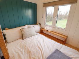 A bed with white bedding next to a window with a view of outside greenery at Shepherds Hut - Oak in Temple Bruer near Lincoln