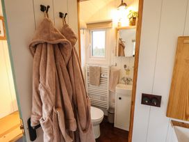 A small bathroom with two robes hanging on the door a toilet a sink with a mirror above and a window at Shepherds Hut - Oak in Temple Bruer near Lincoln