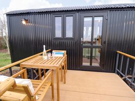 An outdoor deck with wooden table and chairs in front of a black corrugated metal structure at Shepherds Hut - Oak in Temple Bruer near Lincoln