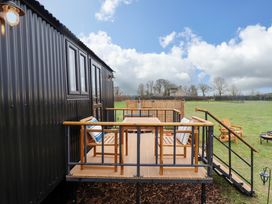 A wooden deck with chairs and table attached to a black cabin in a grassy field at Shepherds Hut - Oak in Temple Bruer near Lincoln