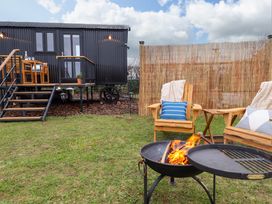 An outdoor area with a black shepherds hut on wheels wooden chairs a fire pit and a bamboo privacy screen at Shepherds Hut - Oak Temple Bruer near Lincoln