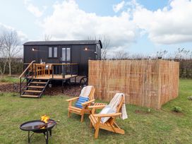 A black shepherds hut with a wooden deck table and chairs and two wooden chairs with cushions and blankets near a fire pit at Shepherds Hut - Oak in Temple Bruer near Lincoln