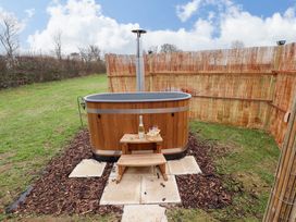 A wooden hot tub with a small wooden stool holding a bottle and glasses outdoors enclosed by a bamboo fence at Shepherds Hut - Oak Temple Bruer near Lincoln