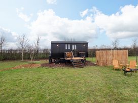 A small black shepherds hut with stairs and a deck in a grassy field with two wooden chairs and fire pit at Shepherds Hut - Oak Temple Bruer near Lincoln