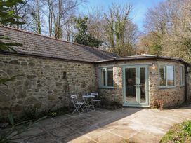 An outdoor stone patio with two white chairs and a small table in front of a stone building with blue framed windows and doors at Rose Cottage in Callington