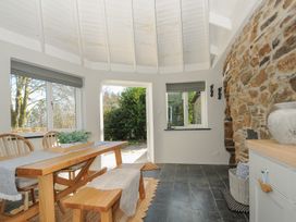 A dining area with wooden table and bench near an open door with stone wall and slate floor at Rose Cottage in Callington
