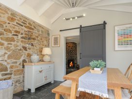 A dining area with a wooden table and bench next to a sliding barn door revealing a room with a fireplace at Rose Cottage in Callington
