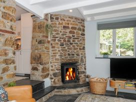 A living room with a stone fireplace a wood-burning stove a TV on a wooden stand and a basket of firewood at Rose Cottage in Callington
