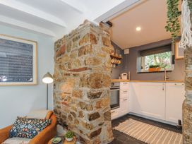 A kitchen with white cabinets and a stone wall next to a leather chair with a pillow at Rose Cottage in Callington