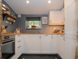 A kitchen with white cabinets wooden countertops a window above the sink and appliances at Rose Cottage in Callington