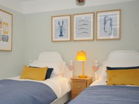 A bedroom with two single beds a wooden nightstand with a yellow lamp and framed pictures of sea creatures on the wall at Rose Cottage in Callington