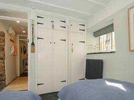 A bedroom with twin beds blue bedding white wardrobes window with fish decorations and a hallway with coat hooks at Rose Cottage in Callington