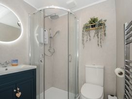 A bathroom with a shower enclosure a toilet a sink with a cabinet a round mirror and a plant on the wall at Rose Cottage in Callington