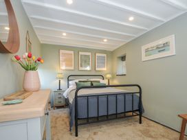 A bedroom with a black metal bed frame a wooden dresser with flowers and three framed pictures above the bed at Rose Cottage in Callington