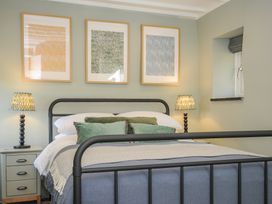 A bedroom with a metal bed frame green cushions bedside tables with lamps and framed artwork above the bed at Rose Cottage in Callington