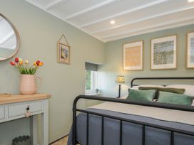 A bedroom with a metal framed bed green cushions and framed pictures above the bed at Rose Cottage in Callington