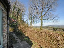 An outdoor path with stone tiles alongside a stone building next to a woven wooden fence and leafless trees at Rose Cottage in Callington