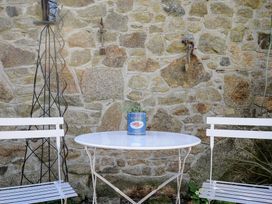 An outdoor seating area with a round white table a plant in a can on the table two white chairs and a stone wall background at Rose Cottage in Callington