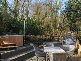 An outdoor wooden deck with a table and four chairs a hanging chair and a hot tub surrounded by trees at Rose Cottage in Callington