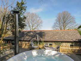 An outdoor deck area with a hot tub table and chairs surrounded by wooden fencing and trees at Rose Cottage in Callington