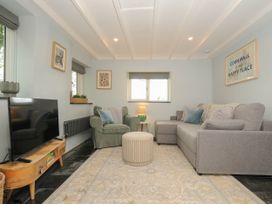 A living room with a grey sofa, green armchair, round ottoman, wooden TV stand, and framed art at Rose Cottage in Callington