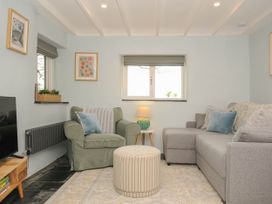 A living room with a green armchair a gray sofa a striped ottoman and a lamp on a small wooden table at Rose Cottage in Callington