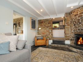 A living room with a gray sofa and leather chair near a stone fireplace and an open doorway to a kitchen at Rose Cottage in Callington