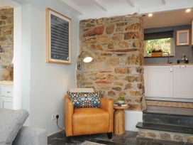 A corner with a leather armchair and decorative pillow next to a stone wall and small wooden side table at Rose Cottage in Callington