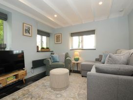 A living room with a gray sofa a green armchair a round ottoman and a wooden TV stand at Rose Cottage in Callington