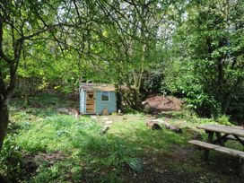 A small wooden playhouse with a heart-shaped cutout in a garden surrounded by trees and a wooden picnic table at Rose Cottage in Callington