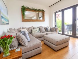 A living room with a gray sectional sofa and matching ottoman by glass doors with a wooden side table with red tulips and a large mirror above the sofa at Buzzards View in Dyserth