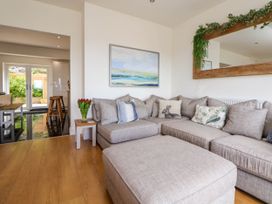 A living room with a large gray sectional sofa wooden floor a side table with red flowers and a painting on the wall at Buzzards View in Dyserth