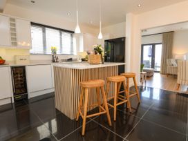 A kitchen with a central island and three wooden stools with a living room visible through an open doorway at Buzzards View in Dyserth