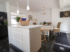 A kitchen and dining area with a white island, wicker chairs, dining table, dartboard on wall and black floor mat at Buzzards View in Dyserth