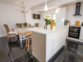 A kitchen with a white island and bar stools next to a dining table with wicker chairs and a dartboard on the wall at Buzzards View in Dyserth
