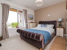 A bedroom with a tufted bed a window with curtains a chest of drawers and a nightstand with a lamp at Buzzards View in Dyserth