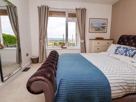 A bedroom with a bed covered in blue and white bedding a chest of drawers a large mirror and a window with curtains at Buzzards View in Dyserth