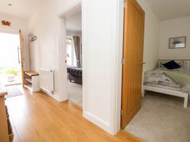 A hallway with wooden floor leading to an open front door and two rooms one with a bed and the other with a sofa at Buzzards View in Dyserth