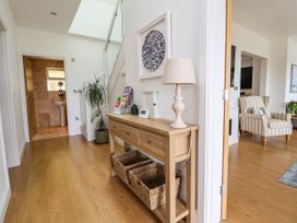 A hallway with wooden floor a wooden console table with a lamp baskets and magazines next to a striped armchair at Buzzards View in Dyserth