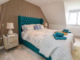 A bedroom with a teal upholstered bed and striped bedding two bedside tables with lamps and a window at Buzzards View in Dyserth