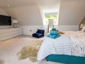 A bedroom with a bed with folded towels a dresser with a lamp a mounted TV a blue chair a mirror and a sheepskin rug at Buzzards View in Dyserth